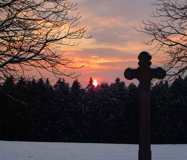 Kreuz mit Wald und Sonnenuntergang im Winter