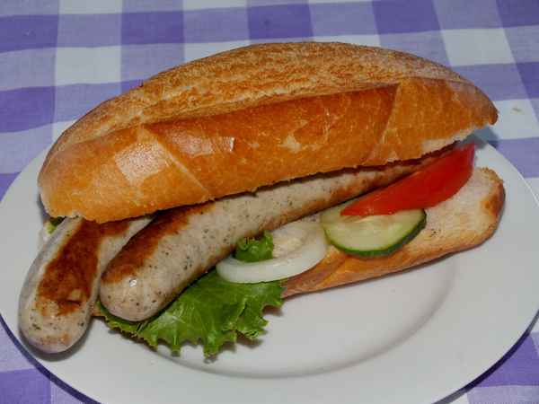Zwei gebratene Würste in Semmel mit Salat auf Teller
