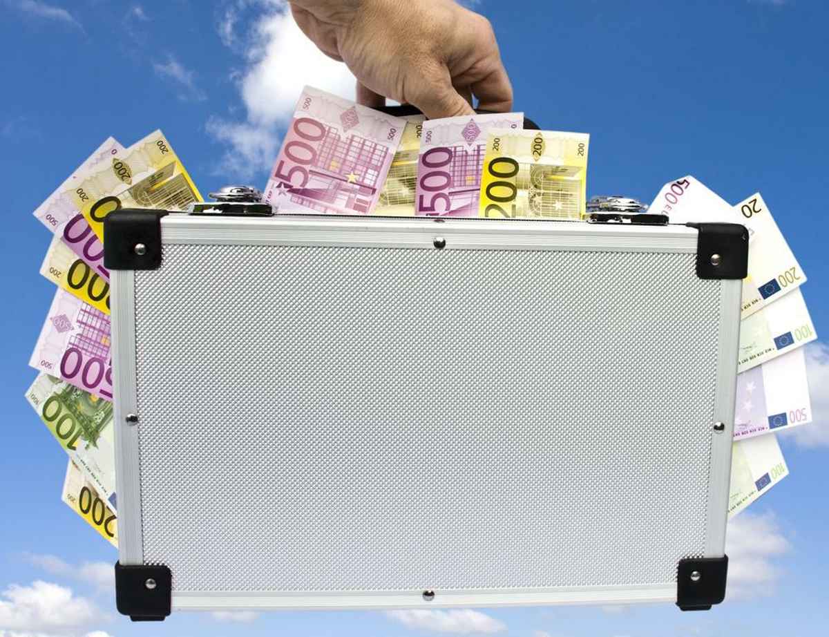 Geldkoffer in der Hand vor Wolkenhintergrund
