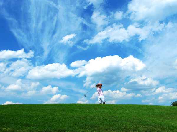 Golferin beim Abschlag vor Wolkenhimmel