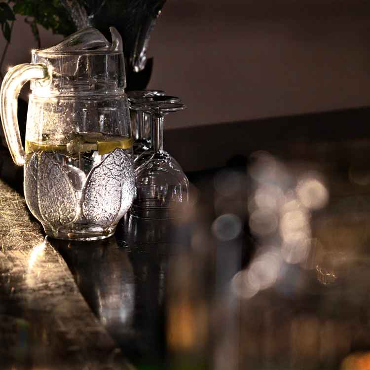 Zitronenwasser im Glaskrug auf alter Holztheke im Sonnenlicht