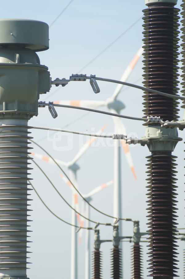 Isolatoren einer Verteilerstation  , im Hintergund Windkraftanlagen