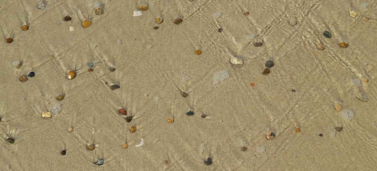 Ablaufendes Meerwasser über Steine und Sand