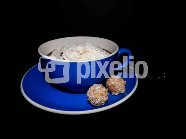 Kaffee in blauer Tasse mit Sahne und Süßigkeit
