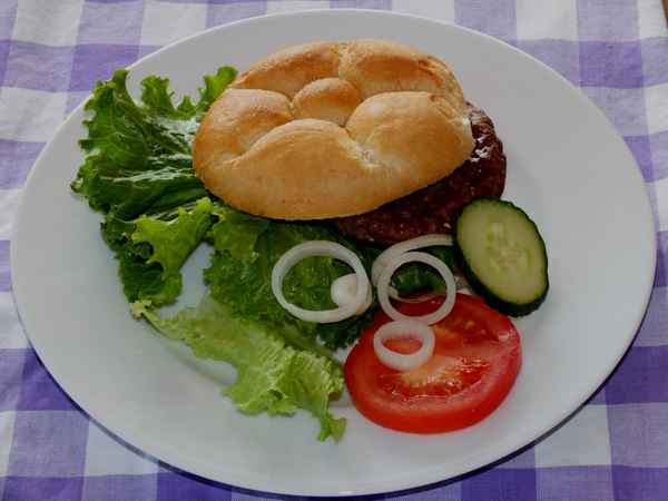 Belegtes Brötchen mit Frikadelle und Beilagen auf Teller